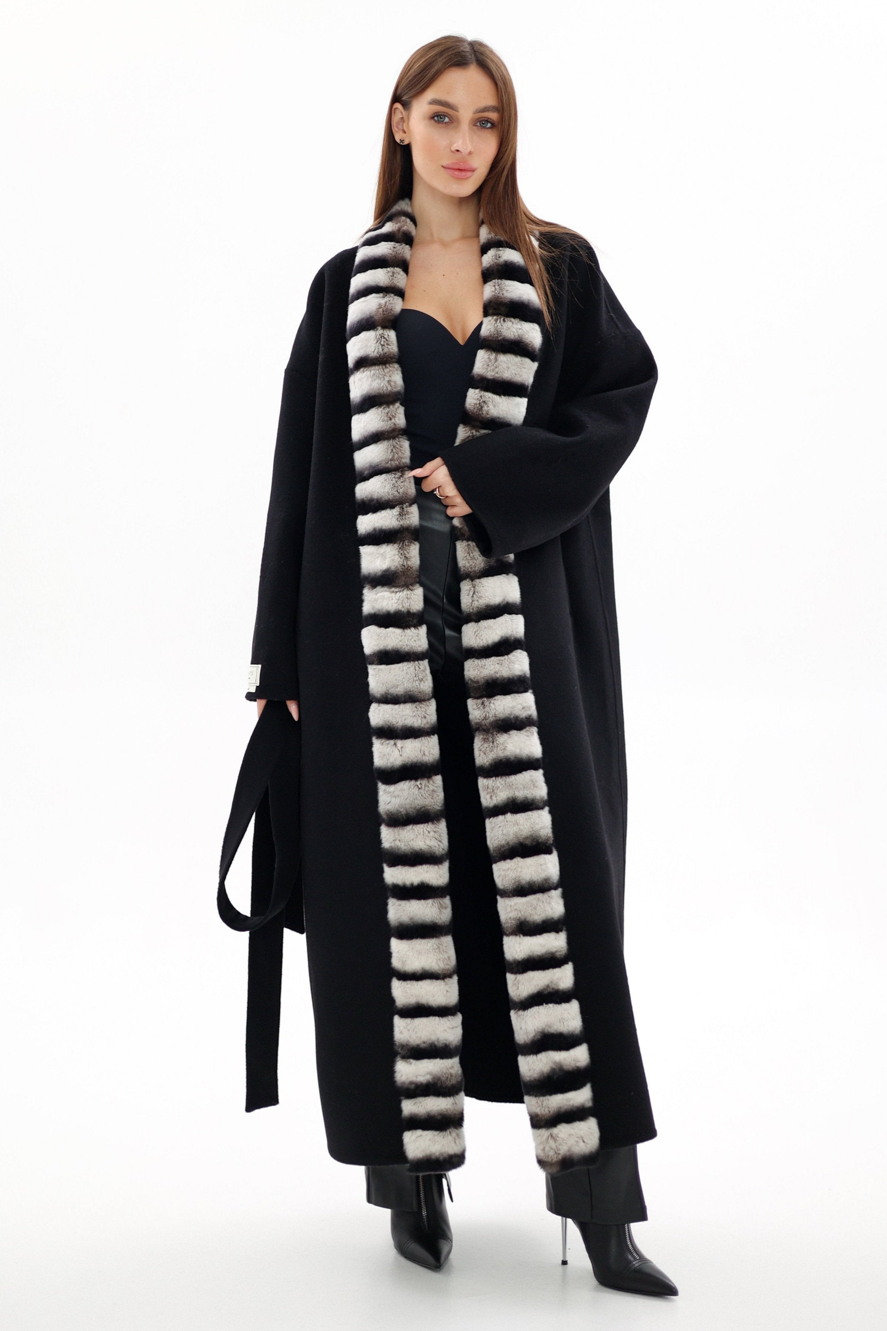 Woman wearing a long black coat with a fur-lined hood on a white background